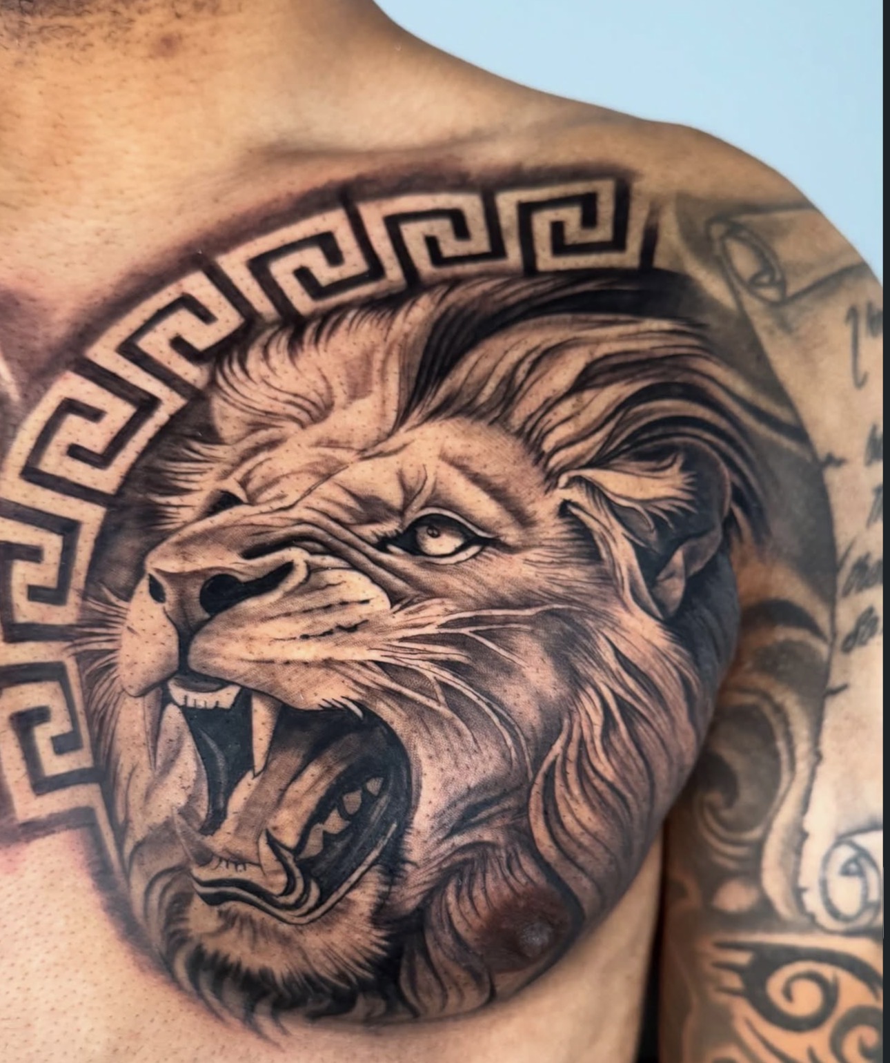 Black and grey roaring lion chest tattoo with Greek key pattern by Sandra